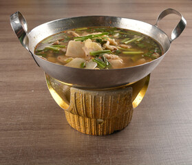 thai clear tom yum spicy chilli hot soup with seafood, meat and vegetables in hot pot in wood...