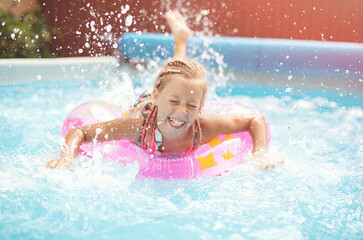 Fototapeta na wymiar Funny little girl swims in a pool in an pink life preserver