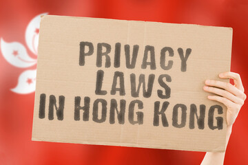 The phrase " Privacy laws in Hong Kong " on a banner in men's hand with blurred Hong Kong flag on the background. Private. Client. Market. Info. Information. Identify. Data. Security. Technology