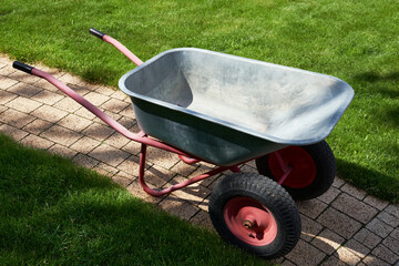 An empty garden wheelbarrow on a paved path among the lawn.