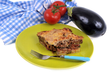Portion de moussaka servie dans une assiette avec une fourchette et ses ingrédients en gros plan sur fond blanc