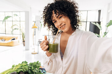 Young african american woman taking selfie drinking green juice reusable bamboo straw