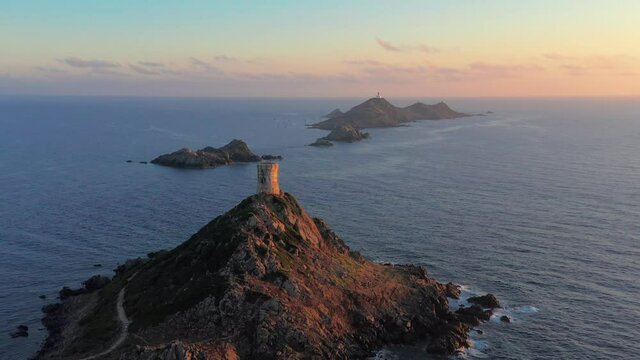 Aerial view lighthouse on mountain rocky hill in sea sunset. Amazing footage of sunrise over the sea during colorful sunset, rocky island,lighthouse on the top of rocky seashore in sundown