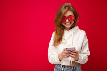 Beautiful young woman wearing casual clothes standing isolated over background surfing on the internet via phone looking at mobile screen