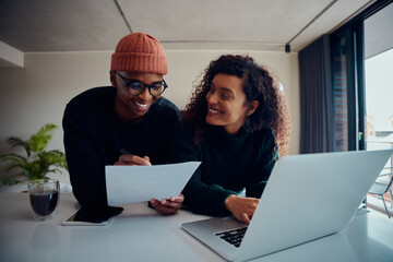 Close up of mixed race couple using laptop for online banking. Happy African American couple smiling and looking at each other while working together at home. High quality photo