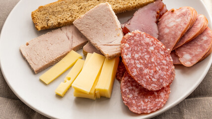 sliced smoked pork, bread, sausage, cheese on plate