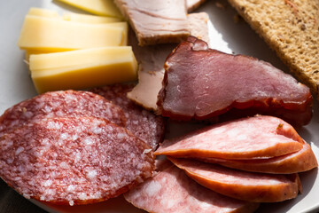 sliced smoked pork, bread, sausage, cheese on plate