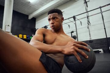 Fototapeta na wymiar African American male doing an intense workout in the gym. Male athlete doing sit-ups with medicine ball. High quality photo