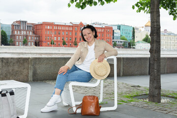 Happy young woman is resting on a bench on the embankment of the Moscow River in summer and smiling.