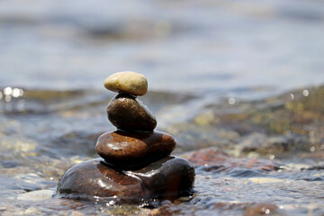 Fototapeta na wymiar Tower of wet pebbles in the sea waves. Summer vacation, beach stones, balance and relax concept