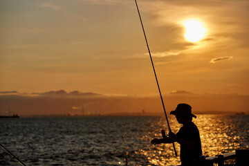 夏の海の海岸で釣りをしている人と鮮やかな夕焼けの風景