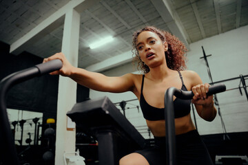 Obraz na płótnie Canvas African American female using an elliptical trainer during cross training. Female athlete working out in the gym. High quality photo