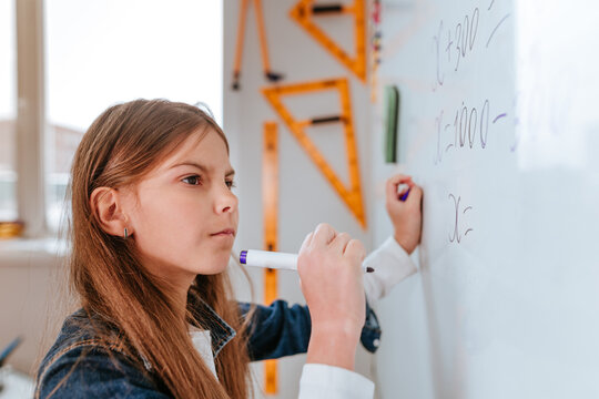 Elementary school student writing on the blackboard by felt-tip in the classroom