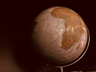 Earth old vintage globe highlighting Africa continent in warm lighting and showing Africa and surrounding continents. Moody cinematic. Vintage globe with africa in focus against dark background.