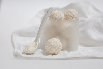 coconut balls on a white table with a white napkin, round sweet candies sprinkled with coconut flakes, vegan dessert