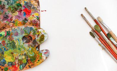 Colorful wooden palette, brushes and paint on a white background. Place for text. Artist's workshop