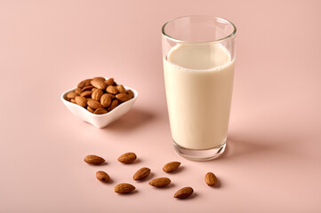 Almond milk in glass and nut seeds on pink powder background. Close up