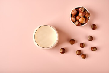 Hazelnut milk in glass and nut seeds on pink powder background. Top view. Copy space