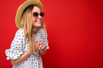 Photo shot of attractive happy smiling young blonde woman wearing summer casual clothes and stylish sunglasses isolated over colorful background wall looking to the side