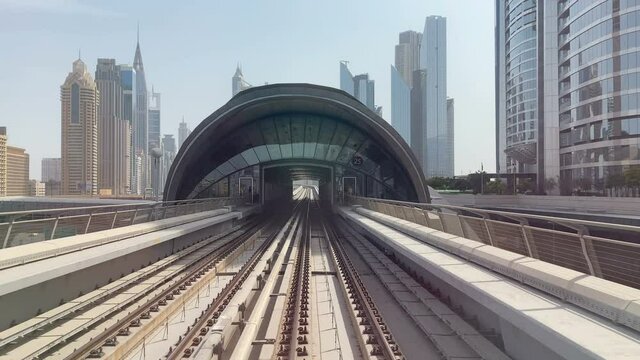 DUBAI, UAE - July 2021. The subway train rides among the glass skyscrapers in Dubai, UAE.The electric train moving outside, driving into a dark tunnel. Planned change of lighting. Unmanned train. View