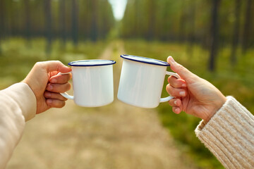 picking season, leisure and people concept - hands of man and woman clinking white tin tea mugs in forest - Powered by Adobe