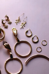 Various gold earrings on pastel pink background. Selective focus.