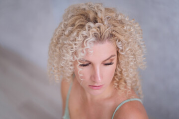 Close-up beauty portrait of caucasian young blonde woman with afro curls hairstyle with blue eyes....