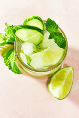 Close-up of the top of mocktail glass with a garnish of fresh cucumber slices, mint, lime on summer detox and refreshment drinks on pink background with sunny daytime shadows.