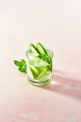 Fresh summer detox and refreshing drinks with cucumber, lime, mint on white wall background. Sunny day shadows from mocktail on pink surface.