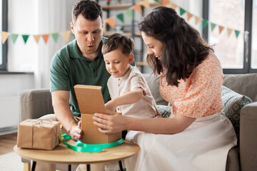 family, holidays and people concept - happy mother, father and little son opening birthday presents at home party