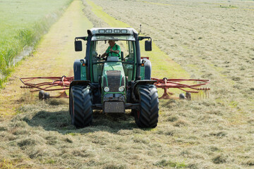 A farmer on a tractor with a machine that collects the hay in rows.