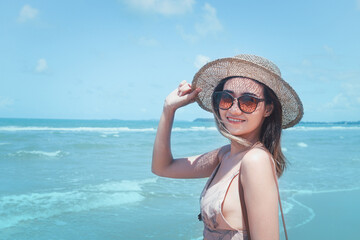 Fototapeta na wymiar Portrait of beautiful Asian woman with big hat and sunglasses enjoy spending time on tropical sand beach blue sea, happy smiling female resting and relaxing on summer holiday vacation.