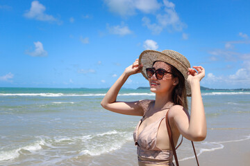 Portrait of beautiful Asian woman with big hat and sunglasses enjoy spending time on tropical sand beach blue sea, happy smiling female resting and relaxing on summer holiday vacation.