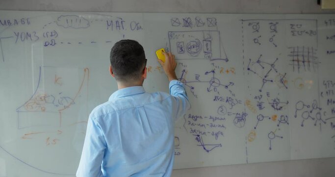 Happy male businessman holding marker, taking notes on white board, smiling businessman writing on whiteboard in office, planning, market analysis, working on project strategy