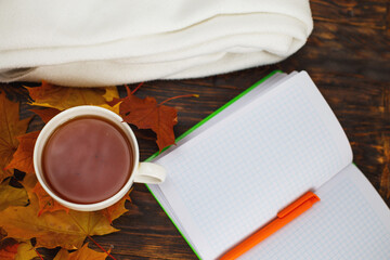 cup of coffee or tea with golden autumn leaves, plaid and notepad on a wooden background .top view. Fall concept.