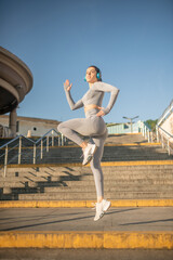 Fit girl in grey sportswear jumping during her warm up exercising