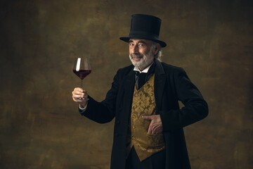 Portrait of elderly gray-haired man, gentleman, aristocrat or actor tasting wine isolated on dark...