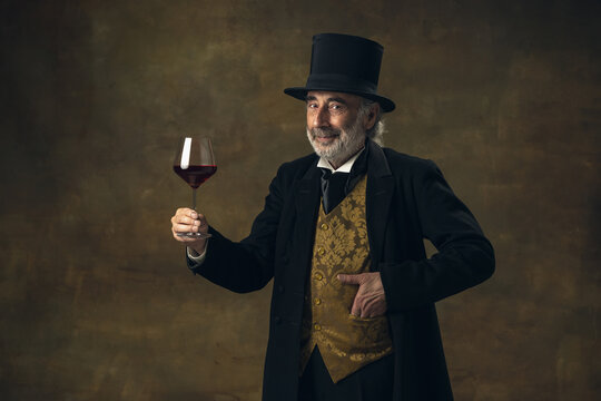 Portrait of elderly gray-haired man, gentleman, aristocrat or actor tasting wine isolated on dark vintage background. Retro style, comparison of eras concept.