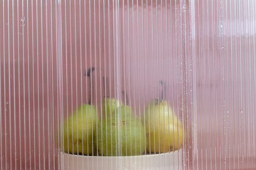 green fresh pears on white podium behind the frozen glass and against brown background
