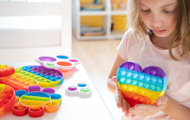 Little girl,kid,child plays with colorful pop it children's room, bedroom.Funny trendy silicone antistress colorful sensory push toy popit.Flapping fidget.Rainbow color.Cure of autism.Stress reliever