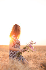 Girl with flowersin hands in a wheat field at sunset