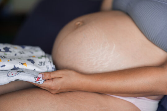 A pregnant woman holds baby diapers in her hands. Pregnant girl's stomach is close-up
