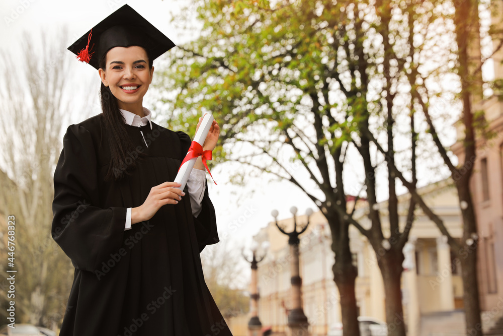 Wall mural Happy student with diploma after graduation ceremony outdoors. Space for text