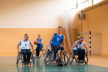 Disabled War veterans mixed race opposing basketball teams in wheelchairs photographed in action while playing an important match in a modern hall. 