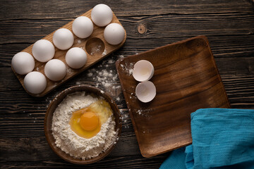 Eggs, flour and wooden dishes on a wooden table and a blue towel