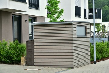 Kombination von Abfall-Sammelbehälter-Einhausung und Geräteunterstand aus imprägniertem Holz vor einem Wohnhaus