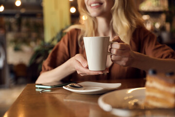 Young woman with cup of coffee at cafe in morning, closeup