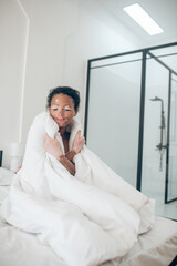 Young woman sitting in bed covered with blanket and feeling relaxed