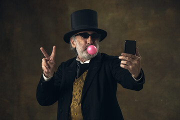 Cute senior man, gentleman, aristocrat or actor having fun isolated on dark vintage background....