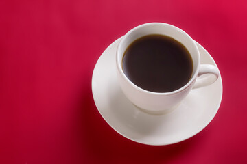 White cup with hot aromatic coffee on a saucer on a red background